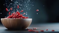 Fresh red goji berries splashing from wooden bowl on dark background with water drops and dramatic lighting, healthy superfood concept.
