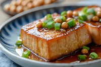Glazed tofu steak with teriyaki sauce and green onions on blue ceramic plate, close up view. Asian cuisine dish garnished with fresh scallions and chickpeas.