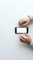 Male hands holding black smartphone with blank white screen on white desk surface for mockup and app presentation purposes.