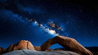 Majestic natural stone arch formation under vibrant Milky Way galaxy at night, dramatic desert landscape with starry sky and illuminated sandstone rock.