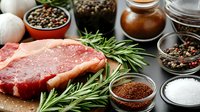 Raw beef steak with fresh rosemary sprigs, colorful peppercorns, sea salt, and aromatic spices on dark background, close up view of meat preparation.