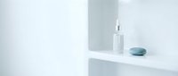 Minimalist skincare display with white dropper bottle and blue stone on floating shelf against clean white wall background.