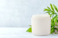 White cosmetic cream jar with green leaves and flowers on light background, natural organic skincare product packaging mockup for beauty and wellness brands.
