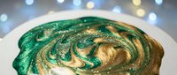 Green and gold swirled frosting with glitter sparkles on cake against bokeh lights background for holiday baking and festive dessert celebrations.