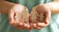 Protective hands holding paper cutout family figures representing care, support and family protection concepts for insurance and social services.
