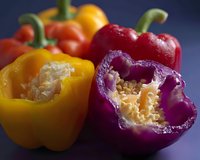 Fresh colorful bell peppers cut in half showing inner seeds and membrane structure against dark background, macro food photography for cooking and recipe blogs.