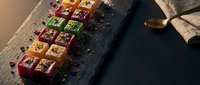 Colorful handmade chocolate pralines with nuts and dried fruits arranged on dark slate board with cocoa powder dusting for gourmet confectionery display.