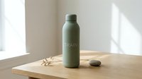 Sage green insulated water bottle with minimalist design on wooden surface with natural light and decorative elements for lifestyle and product photography.