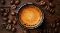 Fresh espresso with golden crema in dark cup surrounded by scattered roasted coffee beans on wooden background, top view macro shot for cafe menu.