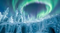 Spectacular aurora borealis dancing over frozen ice castle formations in arctic landscape. Magical northern lights create swirling green patterns above crystalline structures.