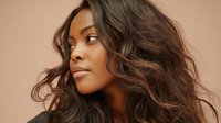 Young woman with flowing wavy brown hair against soft peach background, showcasing natural beauty and elegant profile for fashion or beauty advertising.