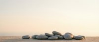 Smooth gray stones arranged on sandy beach at sunset with soft pink sky creating peaceful zen meditation atmosphere for wellness and relaxation concepts.