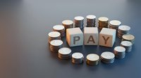 Stacked coins arranged in circle around wooden blocks spelling PAY, representing payment, financial transactions, money management and business costs.