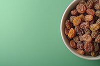 Brown organic raisins in white ceramic bowl on mint green background with copy space for text, healthy dried fruit snack for natural eating.