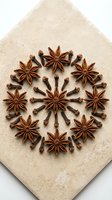 Star anise and cloves arranged in circular mandala pattern on textured beige background for culinary and wellness designs.