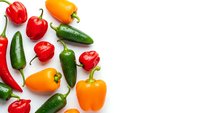 Fresh colorful bell peppers and hot chili peppers scattered on white background. Vibrant red, orange, yellow and green varieties isolated for cooking.