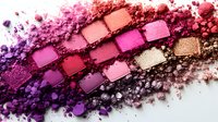 Crushed eyeshadow palette showing gradient from deep purple to pink and coral shades with scattered powder texture on white background. Professional makeup artistry.