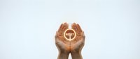 Female hands cupped together holding glowing golden cross symbol against white background representing faith, spirituality and religious devotion.