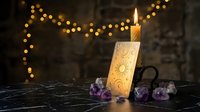 Mystical candle burning with ancient symbols surrounded by purple amethyst crystals and warm bokeh lights creating magical atmosphere for spiritual practices.
