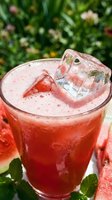 Fresh watermelon juice with ice cubes in a glass, surrounded by sliced watermelon and mint leaves on a sunny summer day.
