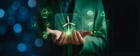 Businessman in green suit holding glowing wind turbine with renewable energy icons floating above hands against dark bokeh background for sustainability concepts.