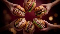 Hands holding assorted gourmet croissant sandwiches with meat, cheese, and fresh vegetables arranged in circle against dark red background with bokeh lights.