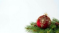 Red ornament with gold filigree design resting on fresh evergreen branches against white background, suitable for holiday and seasonal marketing materials.