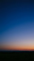 Dramatic twilight sky with deep blue to orange gradient over dark silhouetted landscape horizon for nature backgrounds and atmospheric designs.