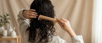 Young woman with long curly dark hair combing wet hair with wooden comb in bathroom. Natural hair care routine and healthy lifestyle concept.