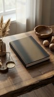 Hardcover book mockup on rustic wooden desk with pampas grass, brass scale, and wooden bowl in warm natural light.