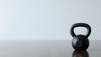 Black kettlebell weight on wooden floor against white wall background for fitness training and strength workout exercises.