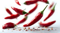 Fresh red chili peppers falling with scattered seeds on white background, creating dynamic composition for food photography and culinary projects.