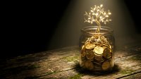 Golden tree growing from coins in glass jar symbolizing financial growth and investment success on wooden surface with warm lighting.