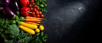Fresh organic vegetables and herbs arranged on dark slate background with copy space for healthy cooking and nutrition concepts.
