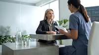 Professional mature Caucasian businesswoman in black suit conducting job interview with young Asian female candidate in modern bright office setting.