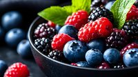 Assorted fresh berries including raspberries, blueberries, and blackberries in dark bowl with green leaves, ideal for healthy eating and food styling projects.