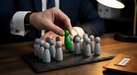 Businessman hand picking green figurine among gray ones on desk, symbolizing leadership, recruitment, and talent selection in business.