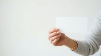 Hand holding blank white card or paper against neutral background, suitable for business cards, gift cards, promotional materials, and marketing presentations.