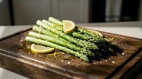 Fresh green asparagus spears with lemon slices and sea salt on rustic wooden cutting board, ready for healthy cooking and gourmet meal preparation.