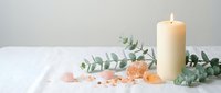 Spa wellness setup with burning candle, pink himalayan salt crystals and fresh eucalyptus branches on white surface for relaxation and aromatherapy.