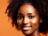 Young African American woman with natural curly hair and radiant smile against orange background showcasing glowing skin and professional makeup application.