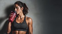 Athletic young woman drinking protein shake after workout in gym with dramatic lighting and copy space for fitness motivation.