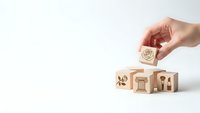 Hand placing wooden cube with heart symbol above blocks showing family icons on white background for insurance and protection concepts.