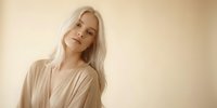 Young blonde woman in beige robe with serene expression against neutral background for wellness and beauty concepts.