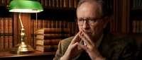 Senior Caucasian businessman in contemplative pose at vintage library desk with banker lamp and leather-bound books for corporate consulting concepts.