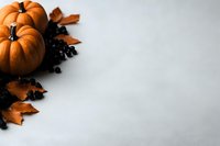 Orange pumpkins with autumn maple leaves and black decorative elements on light gray background with copy space for seasonal holiday designs.