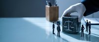 Hand placing miniature courthouse building with tiny business people figures on clean desk surface for legal consulting and justice concepts.