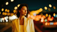 Young Asian businesswoman in white blazer standing on city street at night with bokeh lights background creating warm urban atmosphere.