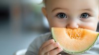 Adorable toddler with blue eyes enjoying fresh cantaloupe melon slice, healthy eating habits and nutrition for children during summer season.