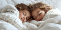 Two young children sleeping peacefully together under cozy white blankets, showcasing innocence and comfort in childhood rest.